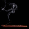 Smoking incense stick on a wooden holder, black background — scent inspiration for Patchouli fragrance oil