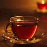 Glass cup of amber tea on a saucer, candlelit — scent inspiration for Pomegranate Cider fragrance oil