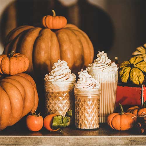 Rustic autumn scene with a jar of pumpkin puree, a small orange pumpkin, cinnamon sticks, and fall leaves on a wooden table—capturing the essence of pumpkin-themed fragrances and treats.