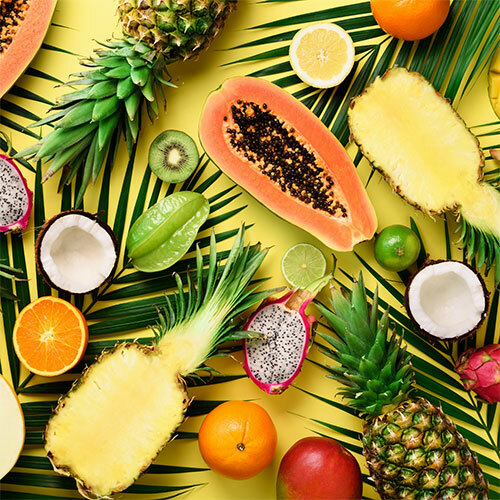 This image features an array of tropical fruits like pineapple, papaya, orange, dragon fruit, and coconuts on a yellow background with palm leaves for added texture and depth.