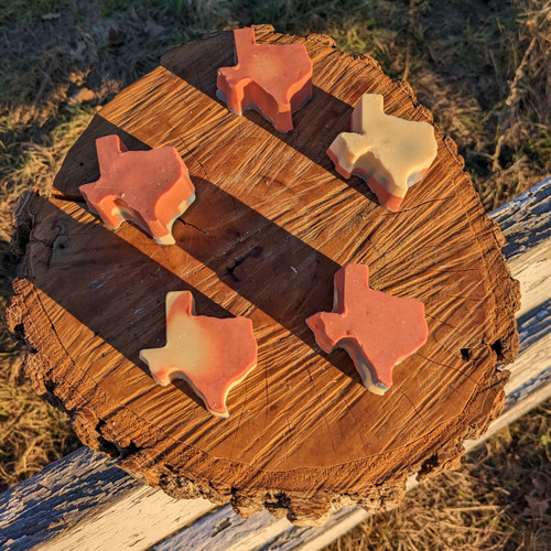 Five small Texas-shaped bars of goat milk soap on a piece of wood.