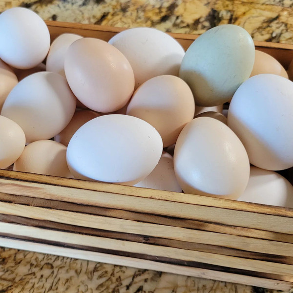 A small wooden crate willed with colorful chicken eggs