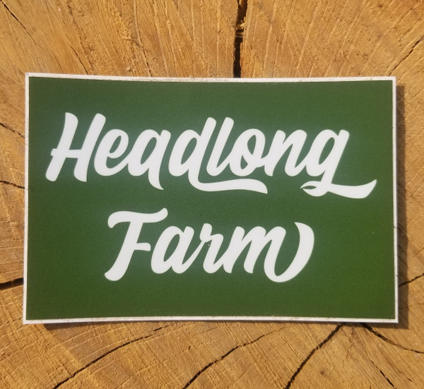 A square wordmark sticker with white text on green background, sitting on a piece of wood