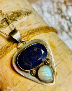"Shop- A captivating two-stone pendant featuring Sapphire and Rainbow Moonstone gems, set within a sterling silver" "Shop- A captivating two-stone pendant featuring Sapphire and Rainbow Moonstone gems, set within a sterling silver"