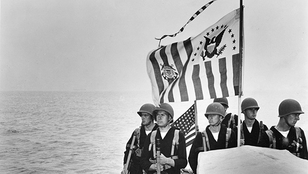 Coast Guardsmen beneath the Coast Guard ensign