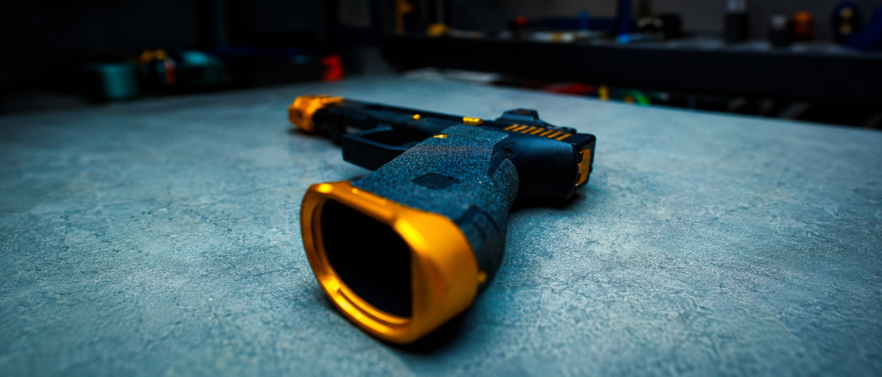 Custom handgun with black Talon Grip and gold magwell on a gunsmith workbench