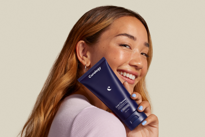 woman holding a bottle of Curology acne cleanser smiling