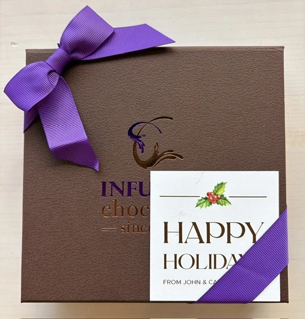 A ribboned Infusion Chocolates gift box with a personalized gift card tucked under the bow