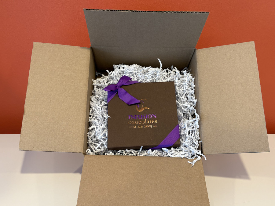 An Infusion Chocolates gift box nested in crinkle paper inside a shipping carton