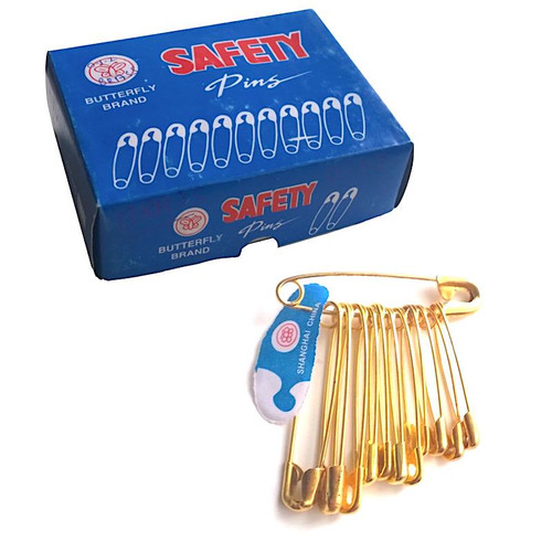 A blue box saying Butterfly Brand Safety Pins and below the box a brass coloured safety pin that is holding 4 small, 4 medium and 3 large brass coloured safety pins