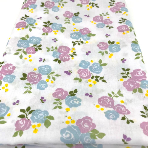 Image shows a white polycotton fabric printed with medium size lilac roses in clusters of three. The floral pattern is evenly spaced, creating a soft, summery look. The fabric is 112cm wide with a smooth finish and shown folded in a rectangle.