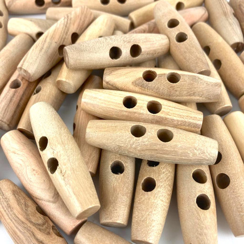 Image shows a handful of large hardwood barrel toggle, approximately 50mm long, with two parallel sewing holes. Smooth, rounded finish suitable for coats and craft projects.