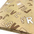 Image shows a lightweight beige cotton fabric with words including “lovely,” “friend,” and “my love” printed in a repeating pattern. The fabric is 137cm wide, soft to the touch, and has a smooth finish with gentle drape. Image shows fabric folded into a rectangle from an angle perspective.