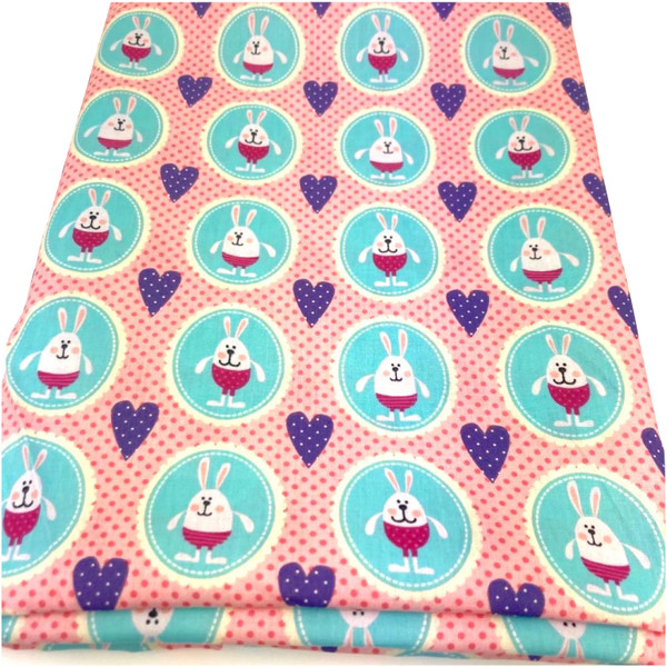 Image shows a lightweight cotton poplin fabric, 147cm wide, with a repeating pattern of happy bunnies and pink dots, purple hearts. The fabric has a smooth, fine weave and a soft drape. The image shows the fabric folded in a rectangle.
