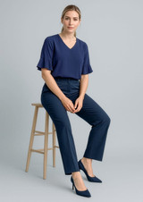 A woman sits on a stool wearing navy blue cool stretch adjustable waist pants and a matching navy top.