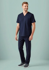 A man wearing a navy scrub top with a V-neck and two front pockets, paired with navy scrub pants.