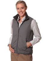 A woman in a grey versatile vest with a zip, paired with a striped shirt, smiling and standing with hands by her side.