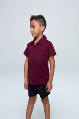 A maroon children's polo shirt with a collar, displayed on a young boy wearing black shorts. The shirt has a logo.