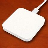 An eco-friendly square wireless charger in a light color with a smooth surface and a connected charging cable.