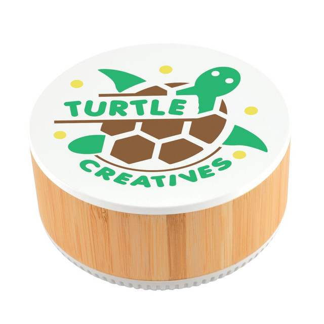 A round speaker made of bamboo with a white top featuring a turtle logo and the text "TURTLE CREATIVES." A round speaker made of bamboo with a white top featuring a turtle logo and the text "TURTLE CREATIVES."