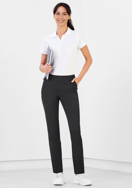 A woman stands wearing black Jane Stretch Pants with a white polo shirt, holding a notebook in a minimalist setting. A woman stands wearing black Jane Stretch Pants with a white polo shirt, holding a notebook in a minimalist setting.