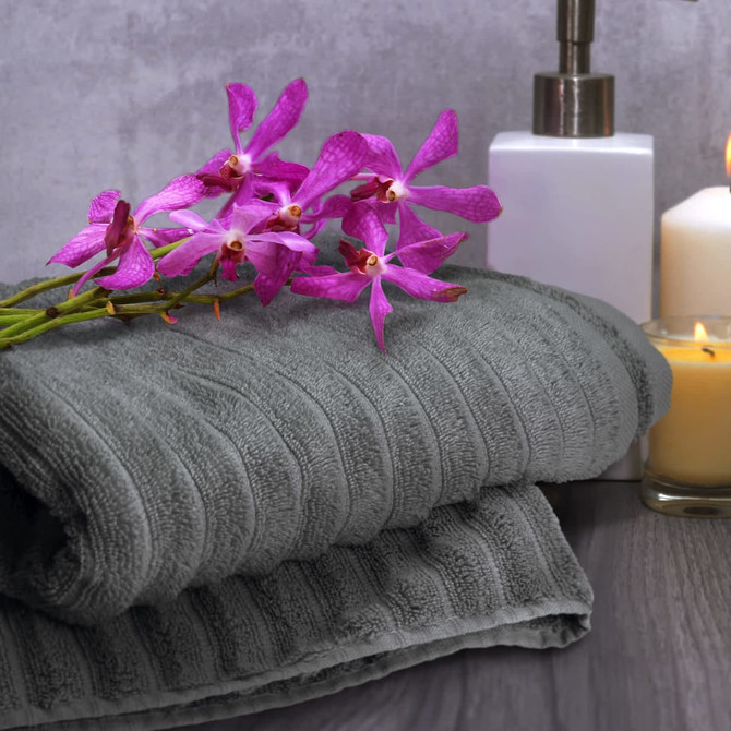 A grey bath towel folded neatly with a bouquet of purple orchids, a white container, and a candle in the background.