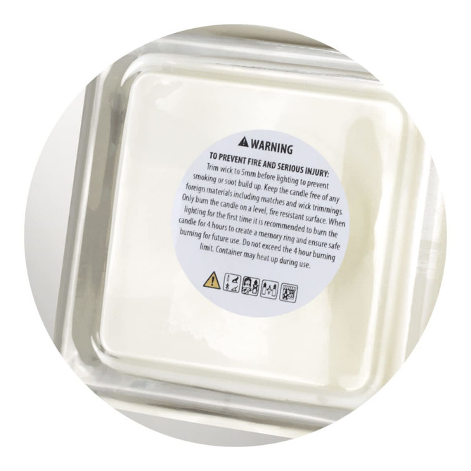 An ambient scented candle in a clear container, featuring a warning label and a white wax interior.