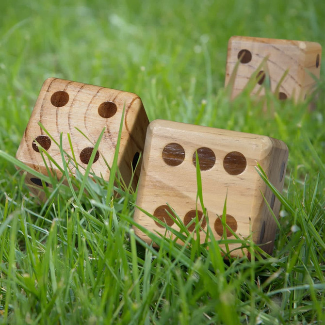 A set of wooden yard dice in natural wood colour, resting on green grass.