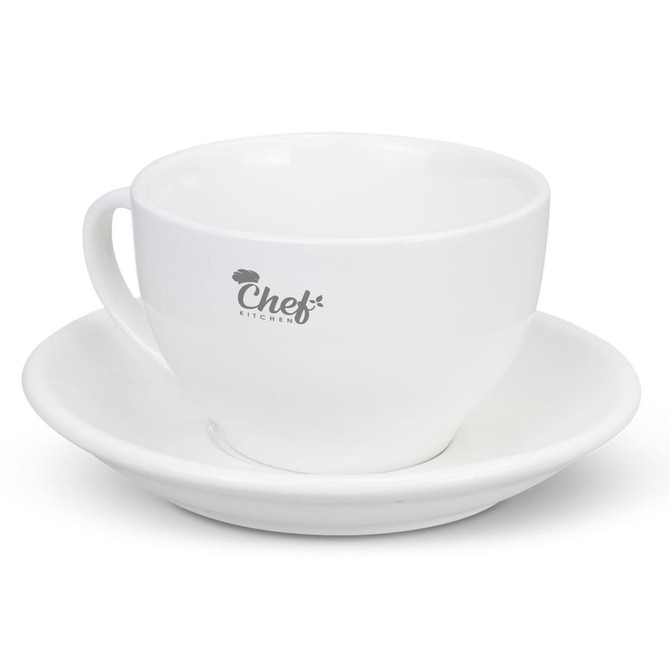 A white chai cup with a matching saucer, featuring a logo on the cup.
