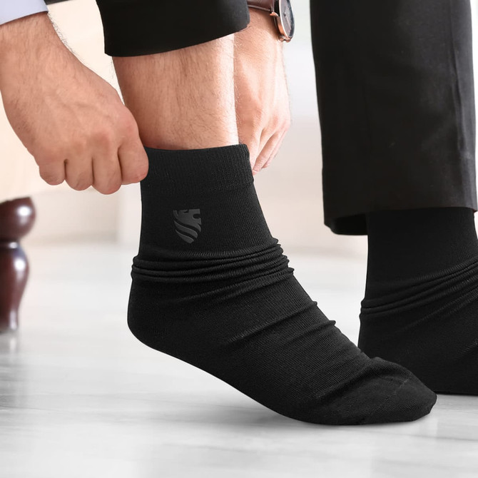 Black socks being worn, featuring a subtle logo on the side. The person is adjusting them while seated.