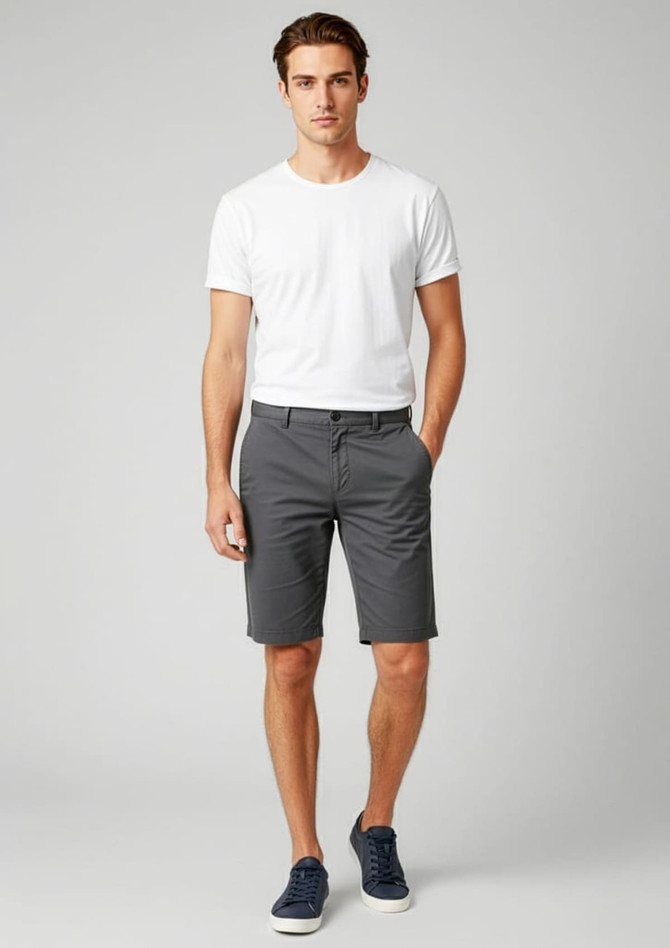 A model wearing grey dress shorts paired with a white t-shirt and navy shoes, featuring a branding logo.