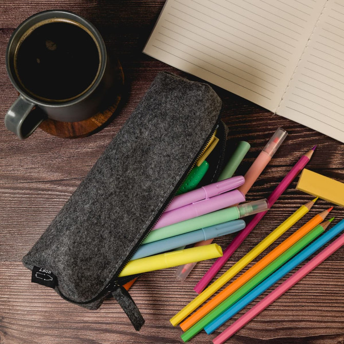 A gray felt utility case surrounded by colorful pens, with a coffee mug and notebook on a wooden surface.