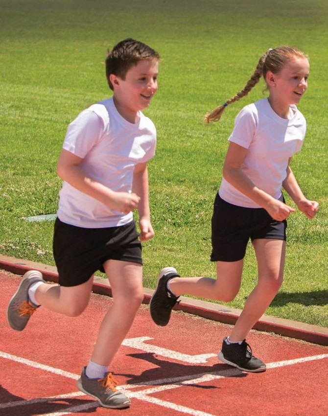 Two children running on a track, wearing white T-shirts and black shorts.