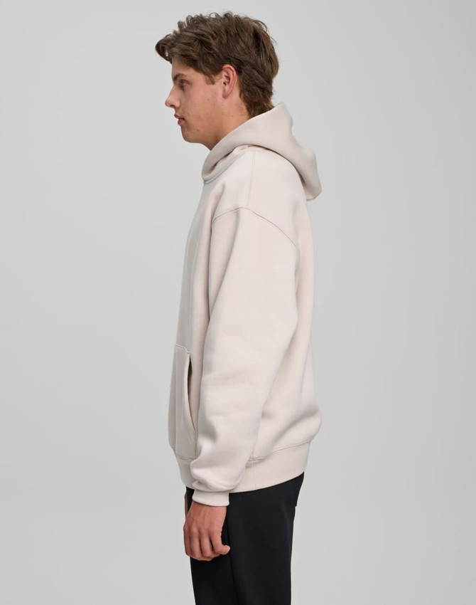 A unisex premium fleece oversized hoodie in light beige, featuring a hood and a front pocket, with a logo visible.