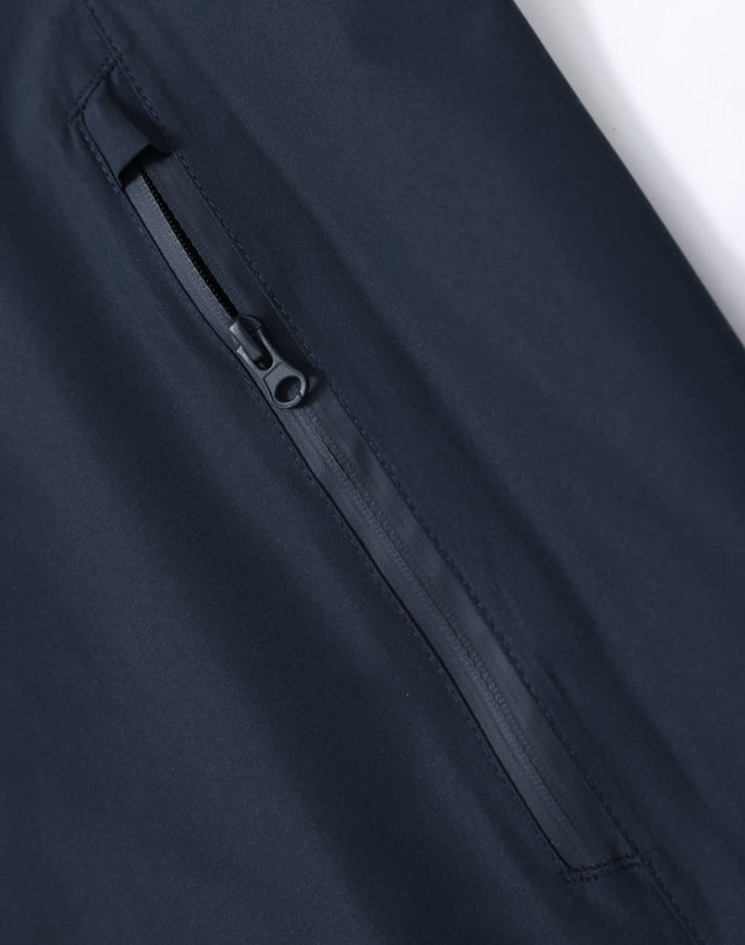 A close-up of a navy waterproof jacket showing a zippered pocket, with a sleek, modern design and a logo.