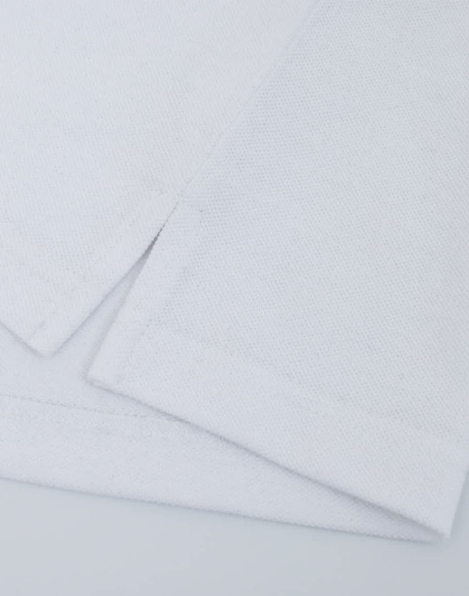 A close-up of a white cotton/poly pique fabric with folded edges, featuring a logo on the corner.