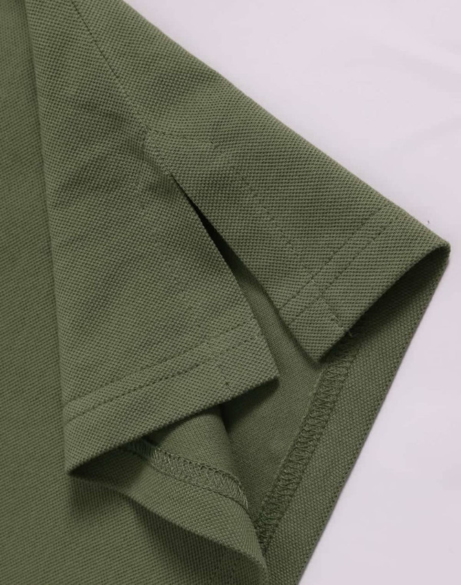 A close-up of a green ultrafine cotton pique polo shirt, highlighting the sleeve and fabric texture.