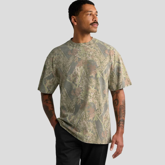 A man wearing a heavy faded camo T-shirt in shades of green and brown, featuring short sleeves and a relaxed fit.