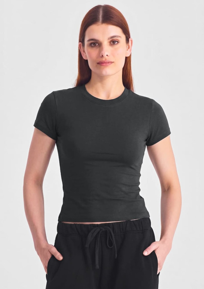 A fitted women's baby tee in dark green with short sleeves, paired with black shorts. It features a subtle logo.