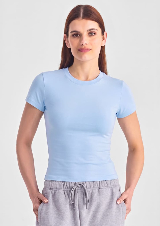 A light blue women's baby tee, featuring short sleeves and a fitted design, worn with grey joggers.