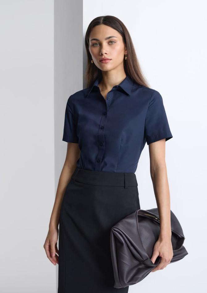 A woman wearing a navy short sleeve shirt, paired with a black skirt and holding a large handbag.