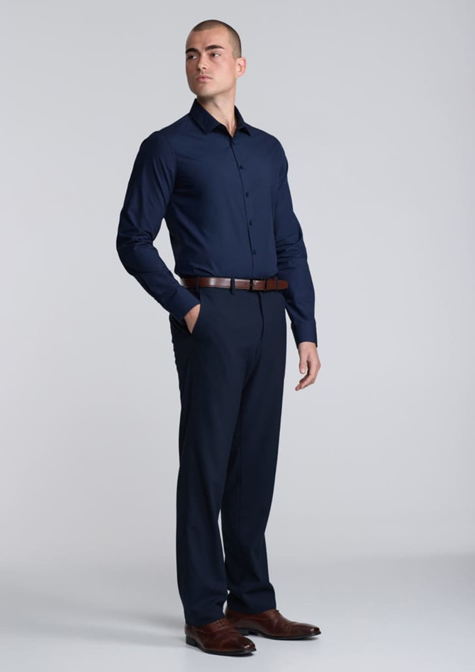 A navy long sleeve shirt is worn by a model, paired with dark trousers and brown shoes. The shirt features a logo.