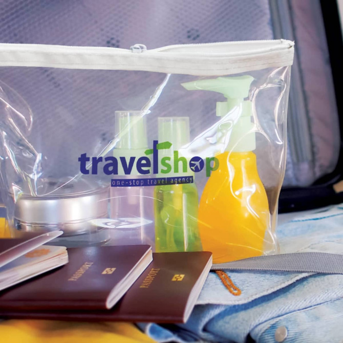 A clear zipper bag containing travel-sized toiletries, including spray bottles, a tin, and passports, against a suitcase background.