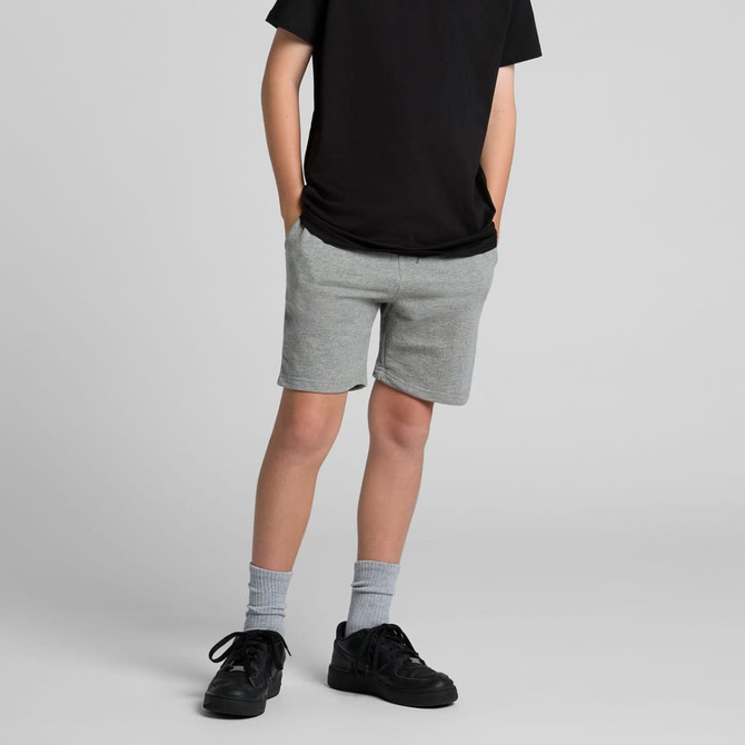 Youth stadium shorts in grey, featuring a comfortable fit and side pockets, worn with a black shirt and sneakers.