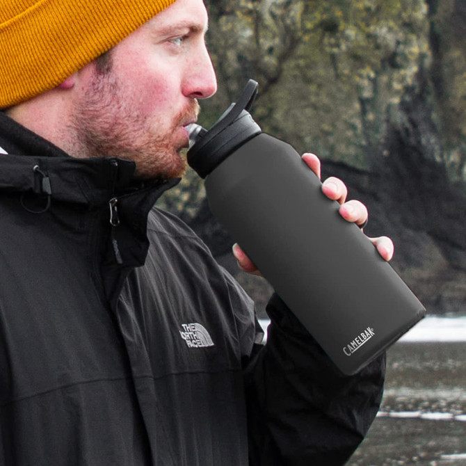 A drink bottle in matte black, featuring a straw lid, held by a person wearing a black jacket and a yellow beanie.