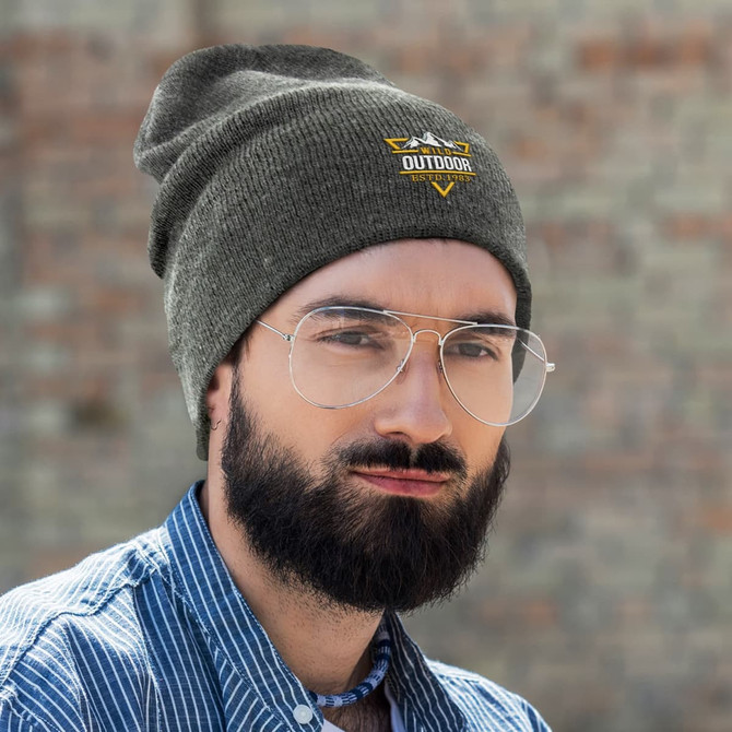 A slouch beanie in olive green, worn by a man with glasses and a beard, featuring a logo on the front.