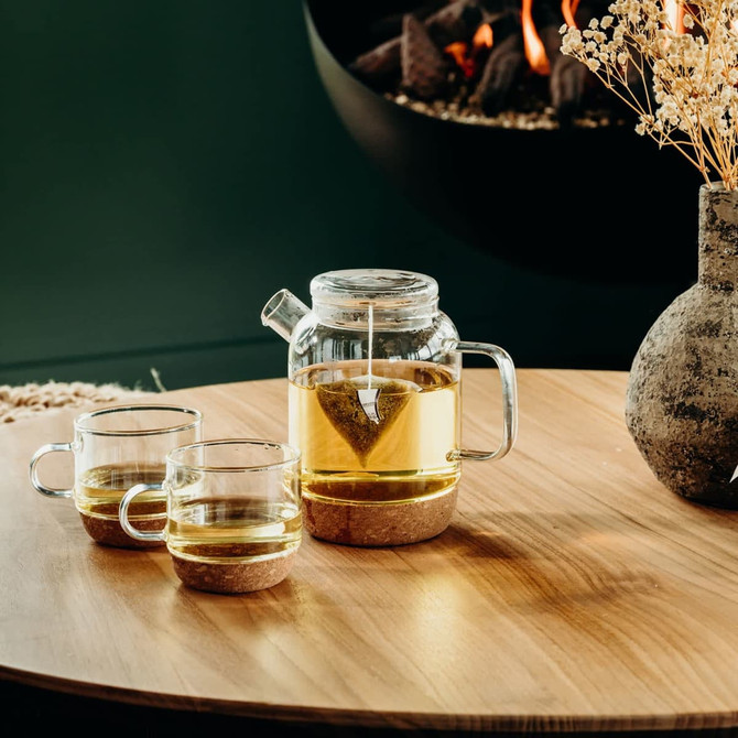A glass teapot with two matching cups featuring cork bases, showcasing a clear and natural aesthetic.
