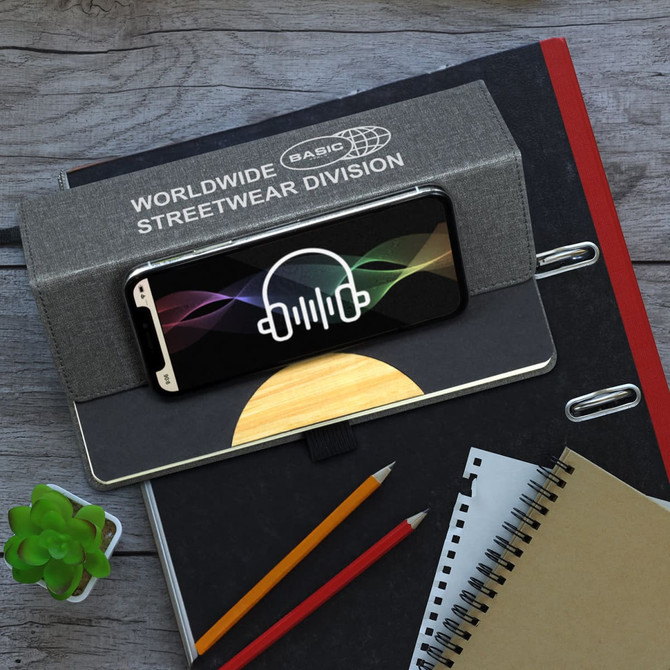 A grey Atoll Notebook with a phone and graphic design on top, alongside a small plant and various stationery items.