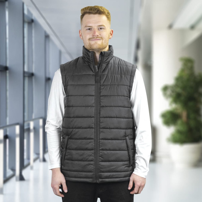A unisex puffer vest in grey, featuring a high collar and a logo, worn over a long-sleeve white top.