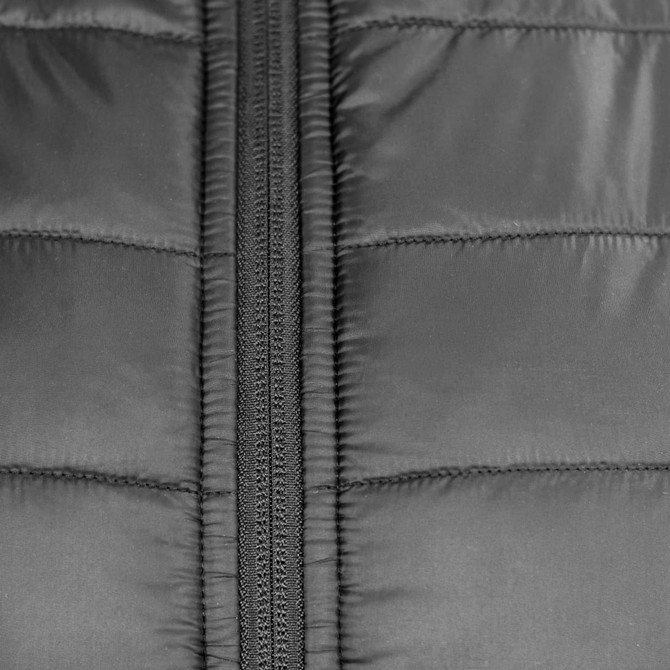 A close-up of a black puffer jacket featuring a zippered front and quilted texture. It has a logo on the fabric.